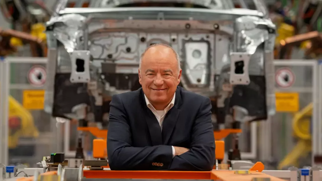A man crosses his arms on a workbench in a car workshop