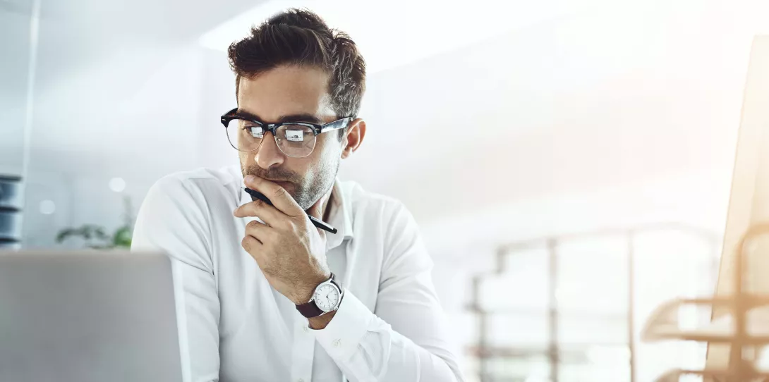 Mann am arbeiten schaut auf seinen Laptop und überlegt