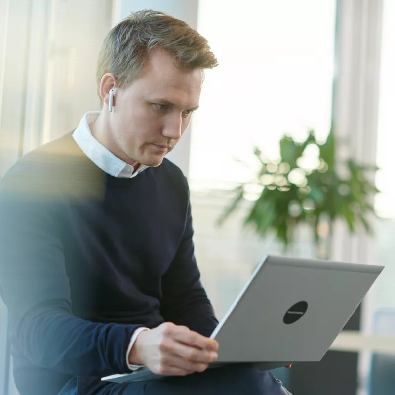 A young man with in-ear headphones works on his laptop