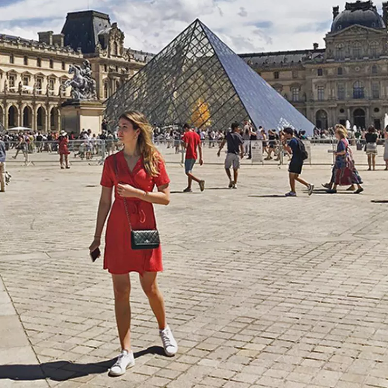 Young woman standing in front of the glass pyramid in the courtyard of the Louvre in Paris
