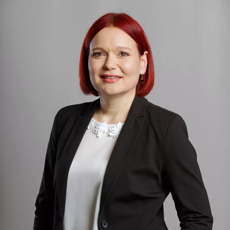 A female consultant in front of a grey background smiles into the camera