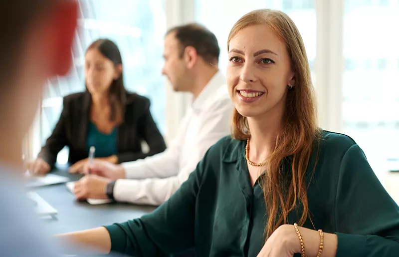 A woman in a green blouse is in an office having a conversation with someone