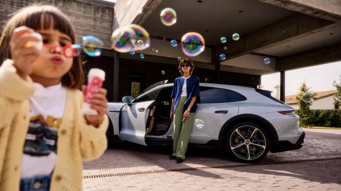 Little girl makes soap bubbles and woman standing in front of a Porsche