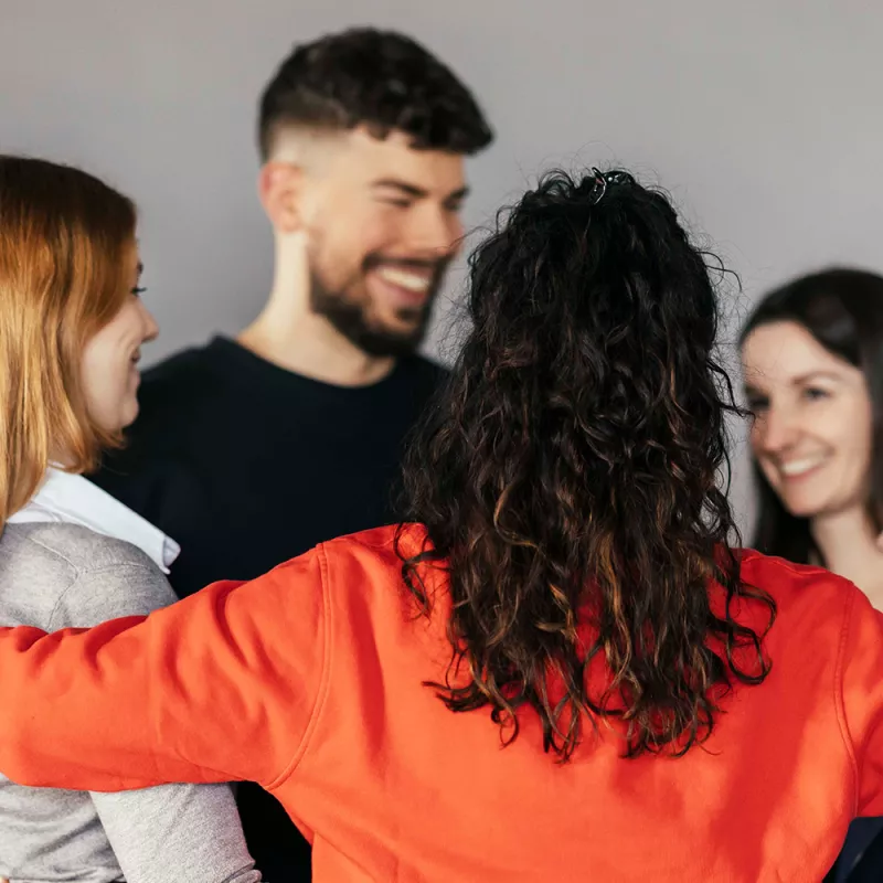 Three women and one man stand together in a circle and smile at each other