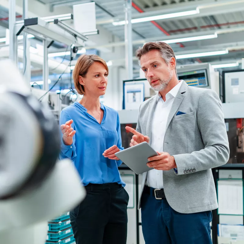 A woman and a man stand in a hall in front of a machine and discuss