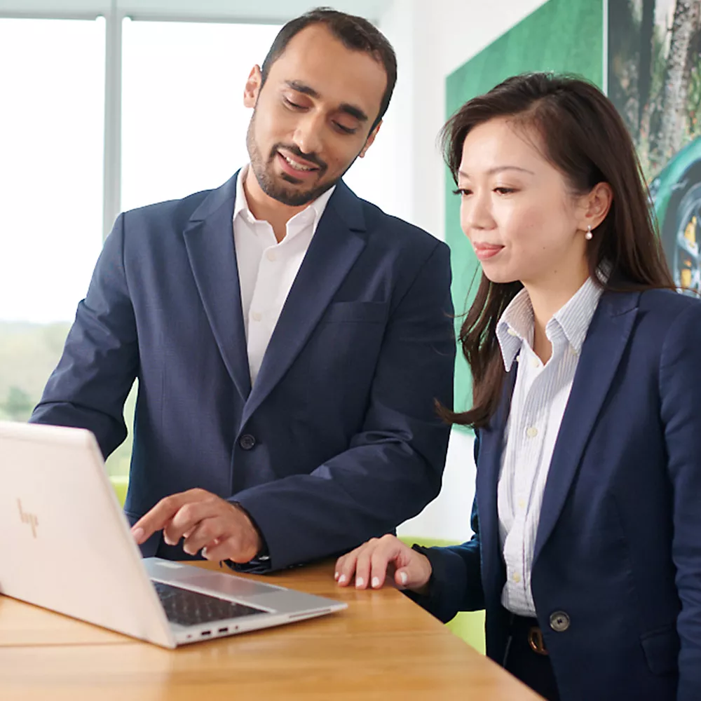 A consultant in a suit shows something on a laptop to his female colleague
