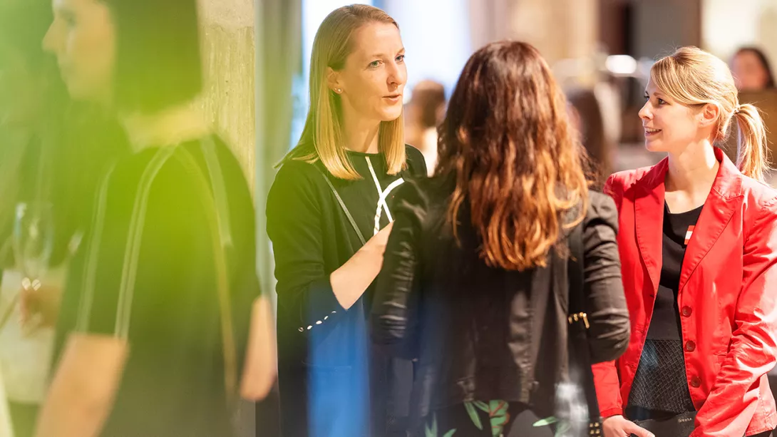 3 female colleagues stand together at an event and talk to each other