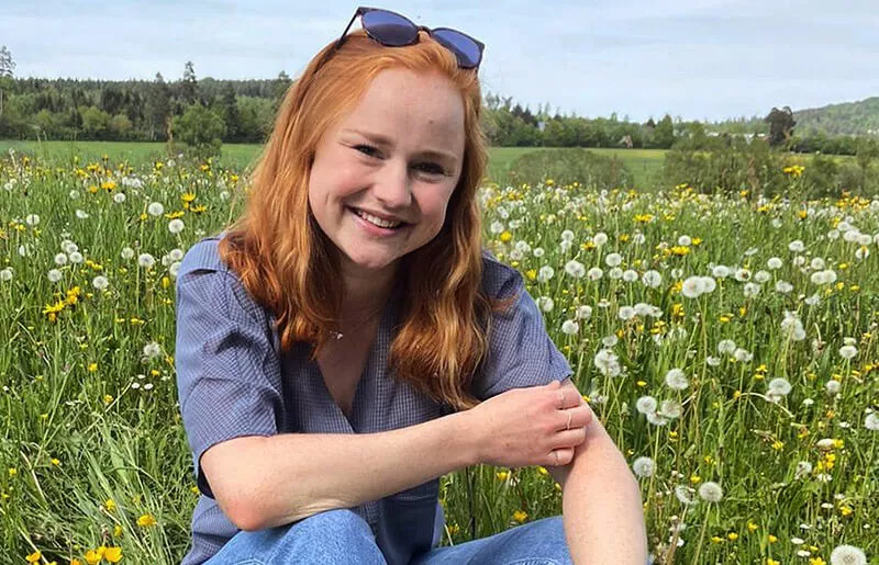 Smiling young woman sitting in a flower meadow with dandelions 