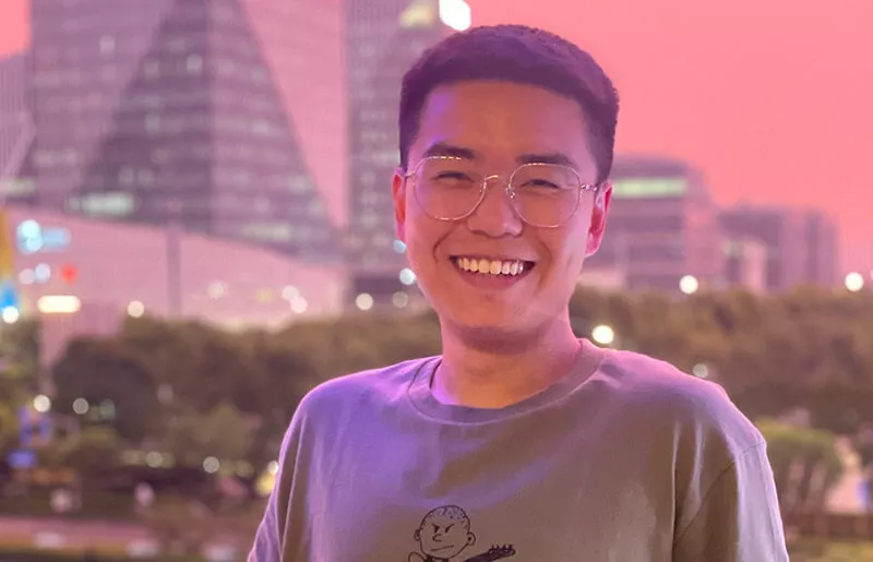 Young man smiling against skyscrapers in the background and a pink sky