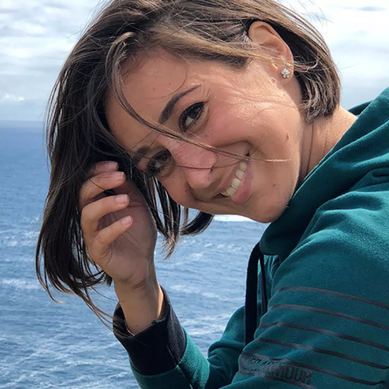Woman laughing into the camera and in the background are sea and a cloudy sky